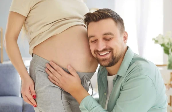 Homem encostando o ouvido na barriga da gestante representando a relação entre epigenética e fertilidade.